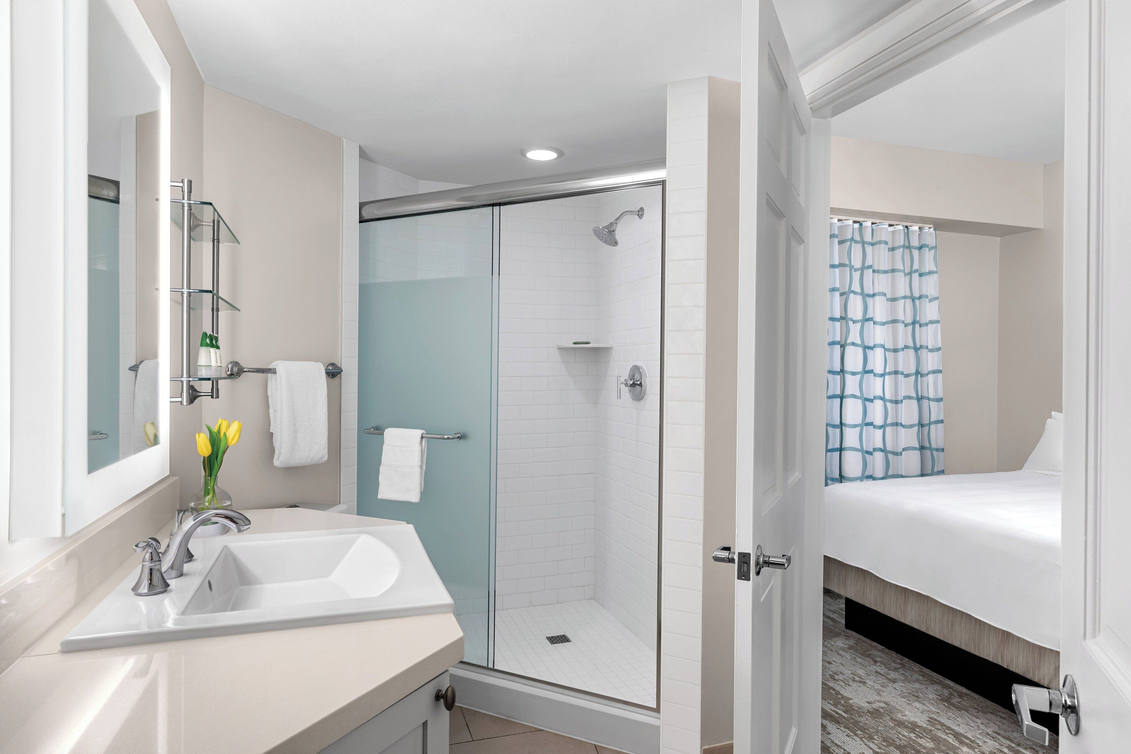 Un baño moderno con ducha envuelta en vidrio, un lavamanos con espejo y una cama con cortina azul.