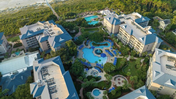 An aerial view of a resort with multiple buildings, a central swimming pool, and a beach in the background. - Marriott's Grande Ocean (Hilton Head Island)