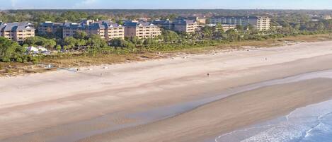 Un hotel frente a la playa con varias edificaciones, una playa de arena y cielo despejado.