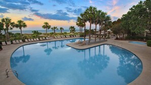 A pool with lounge chairs and palm trees, surrounded by a landscaped area with a view of the ocean. - Marriott's Grande Ocean (Hilton Head Island)
