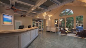 A reception area with a wooden counter, seating area with wicker chairs, large windows, and ceiling fans. - Marriott's Grande Ocean (Hilton Head Island)