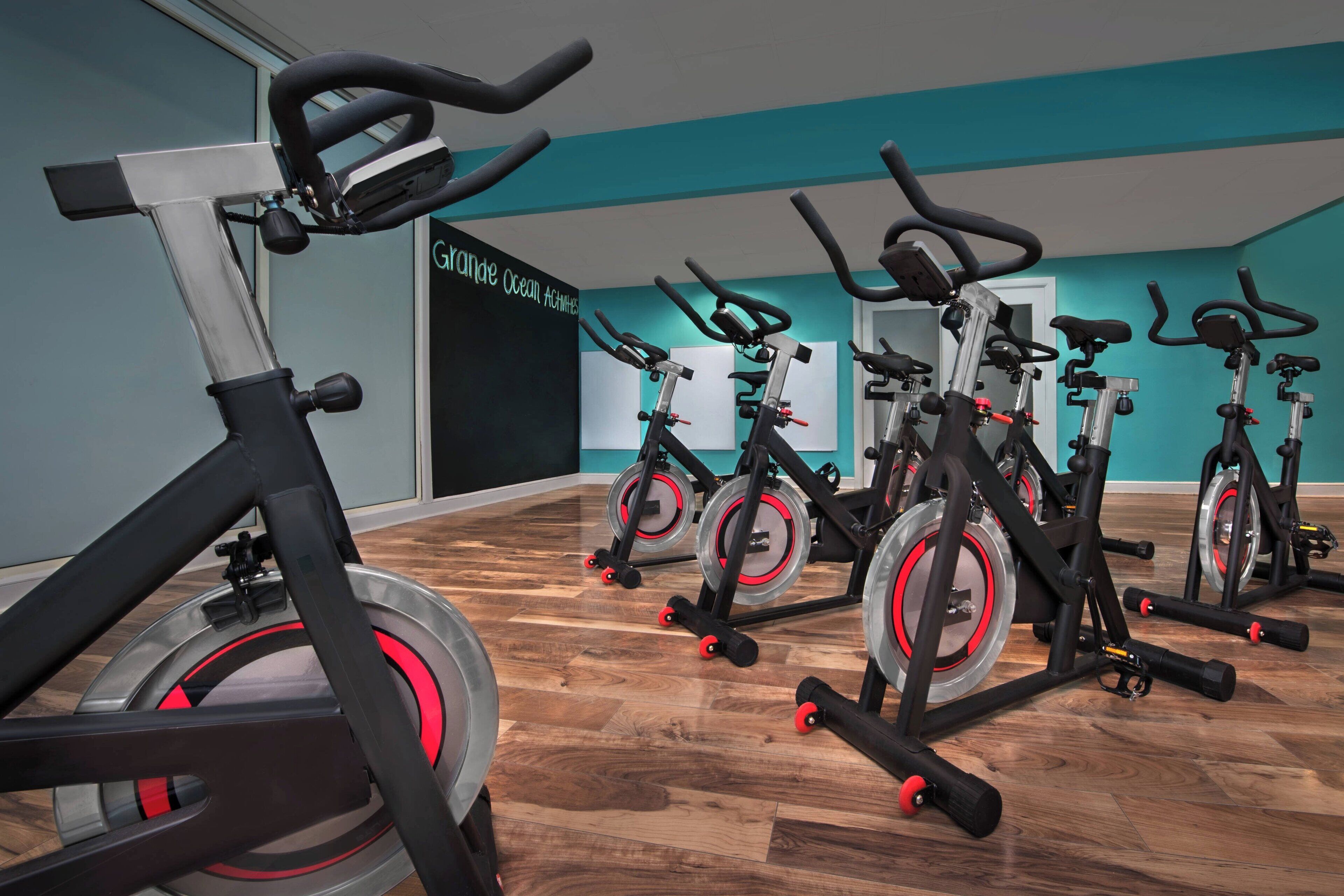 Un gimnasio con bicicletas estáticas dispuestas en filas, una pared color turquesa y un piso de madera.