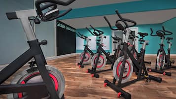 Une salle de sport avec des vélos d’appartement disposés en rangées, un mur de couleur turquoise et un plancher en bois.