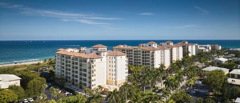 A coastal hotel complex with multiple buildings, a parking area, and palm trees.