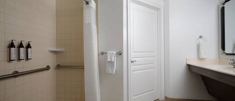 A bathroom with a shower, a white door, a sink with a mirror, and three bottles of shampoo on the wall.