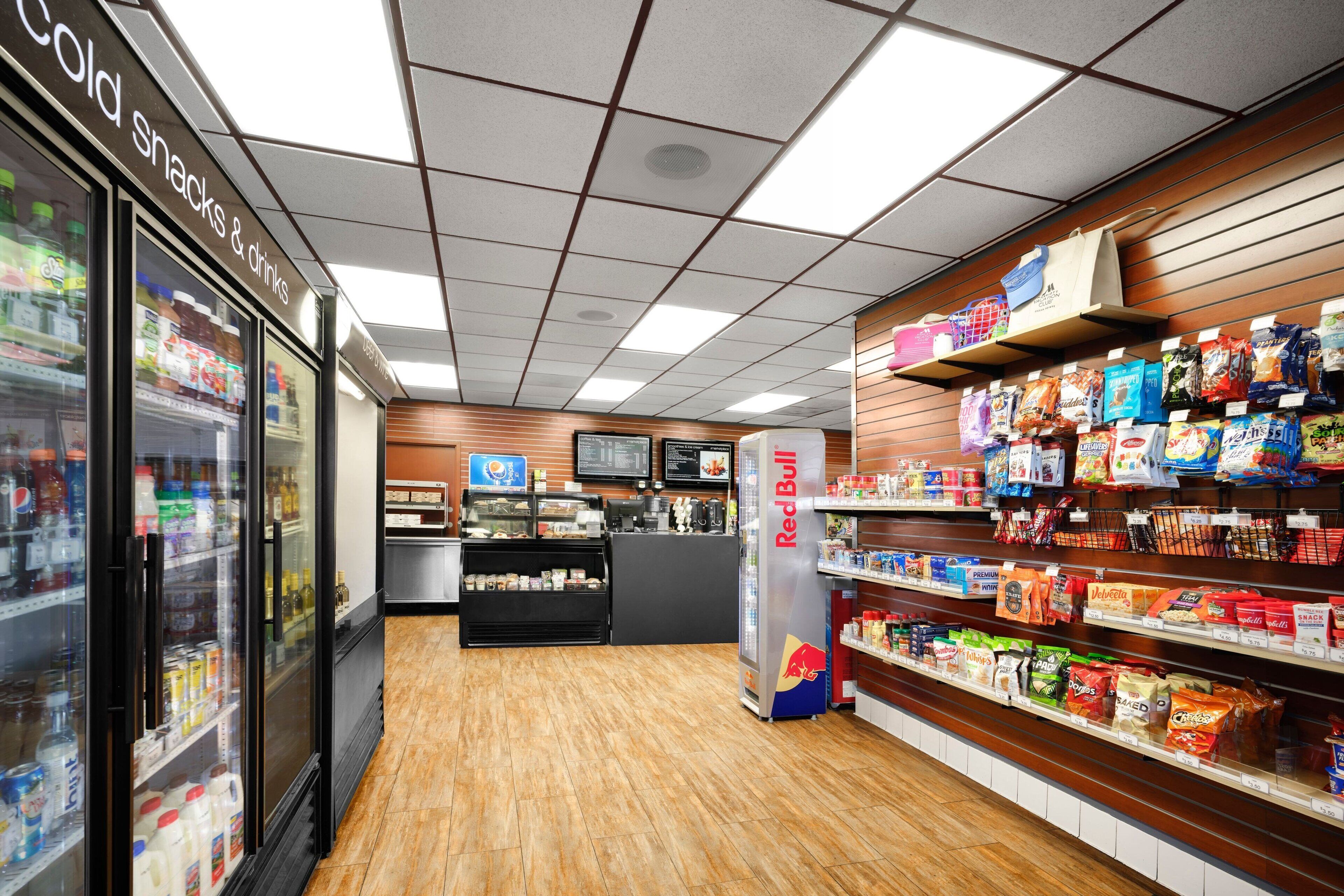 Interior de un supermercado con secciones refrigeradas, un refrigerador de Red Bull y estantes llenos de aperitivos y bebidas.