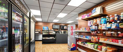 A grocery store interior with refrigerated sections, a Red Bull refrigerator, and shelves stocked with snacks and drinks.