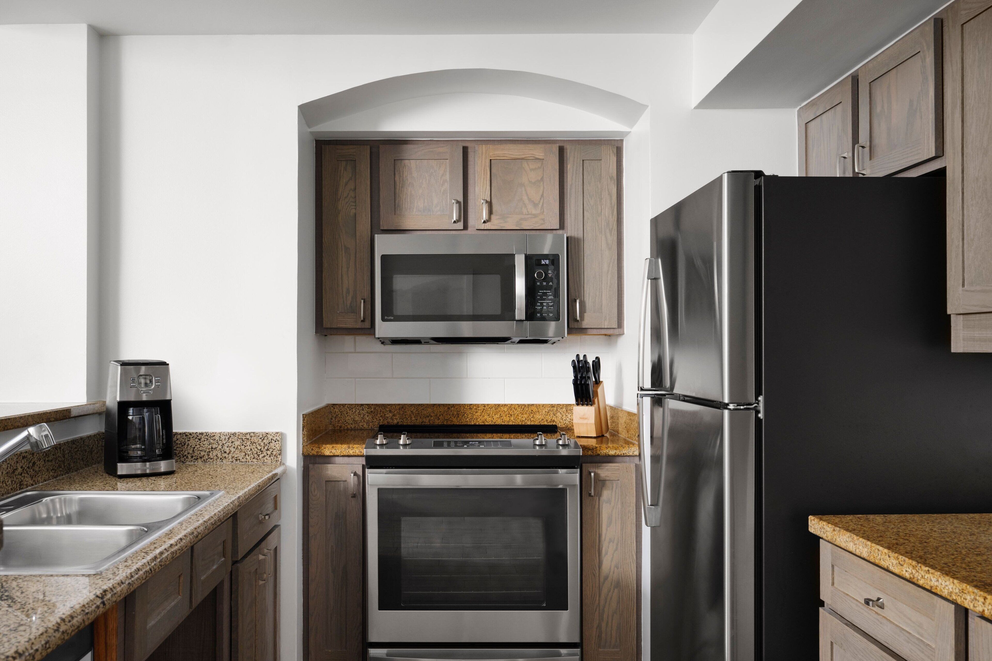 A kitchen with wooden cabinets, a stainless steel refrigerator, a microwave, a coffee maker, and a stove.