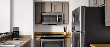 A kitchen with wooden cabinets, a stainless steel refrigerator, a microwave, a coffee maker, and a stove.