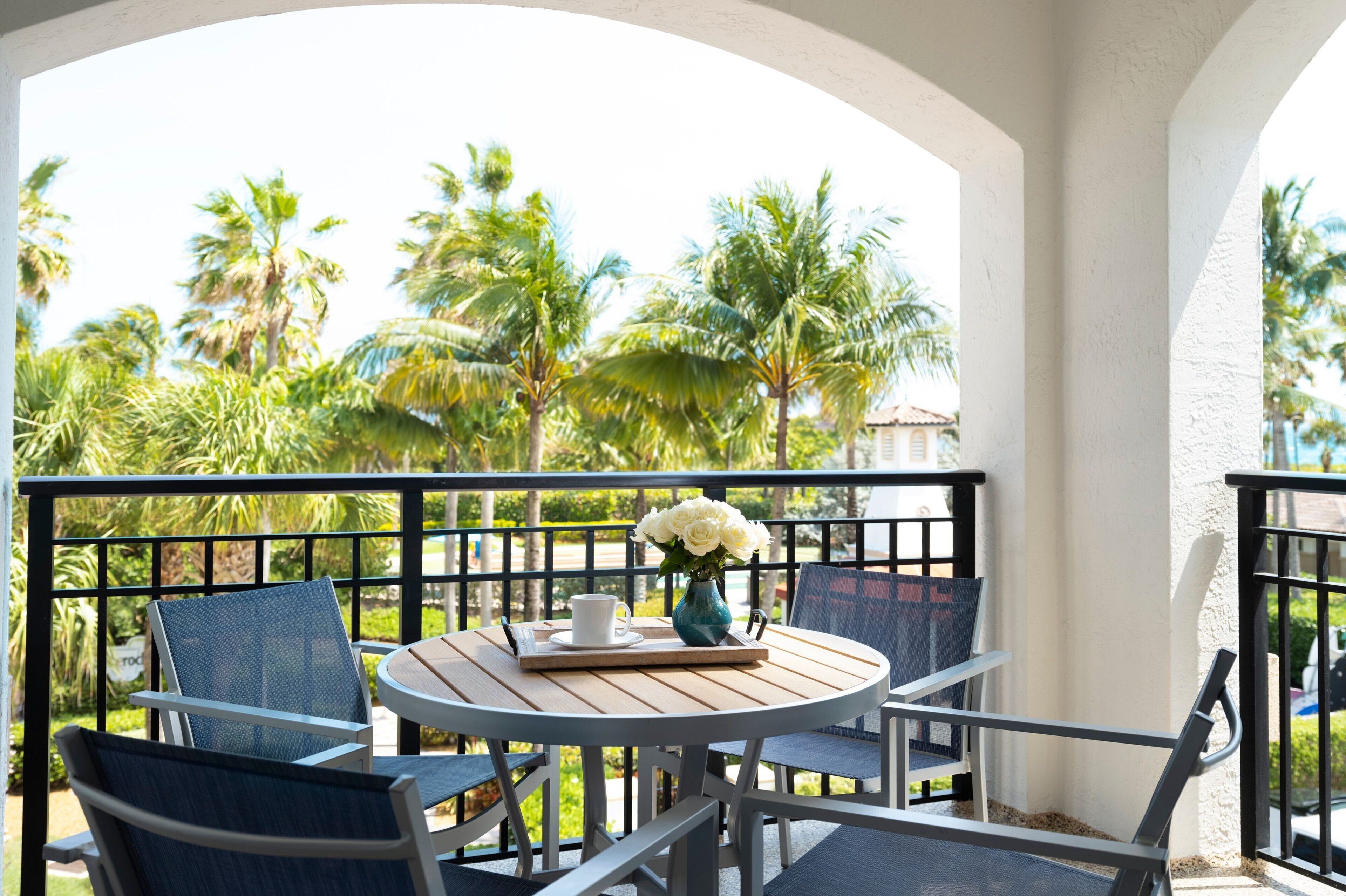 A round table with chairs on a balcony, a vase with flowers, and a tray with a cup and saucer.