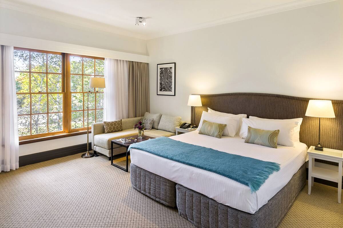Una habitación de hotel con una cama grande, un sofá, una mesa de centro y un ventanal con cortinas.