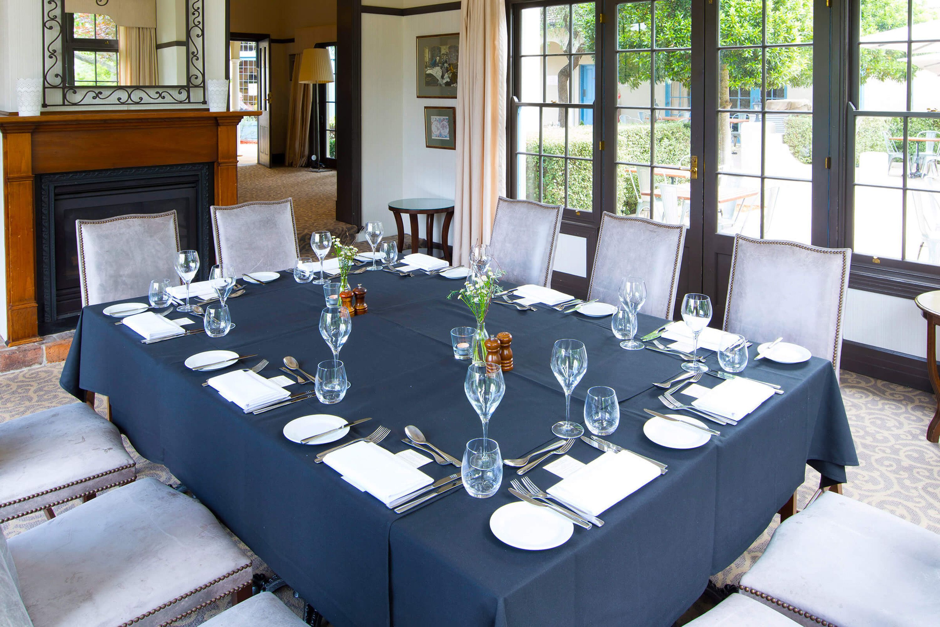 A dining table set for six with white plates, silverware, and clear glasses, surrounded by upholstered chairs.