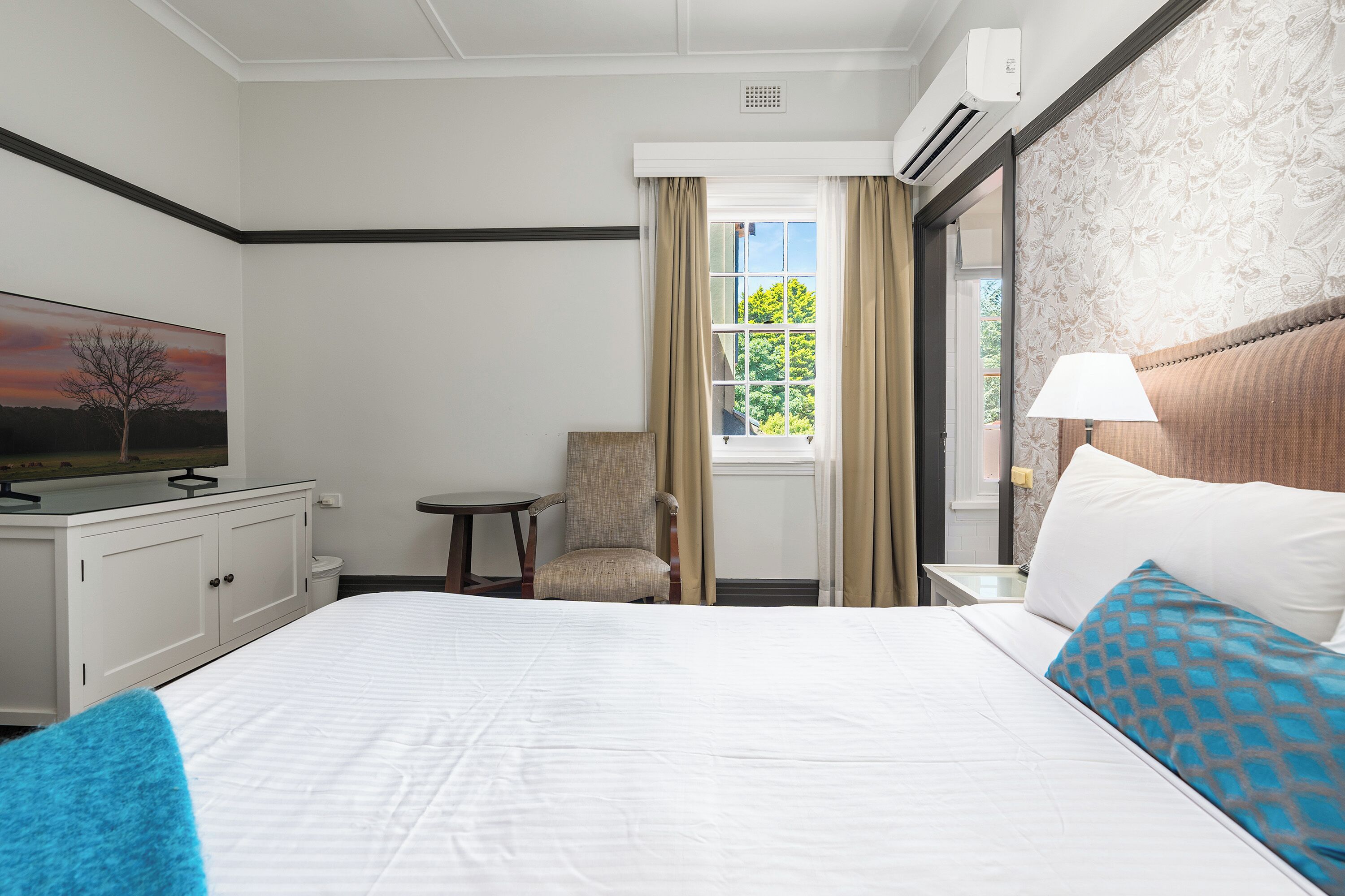 A hotel room with a large bed, a chair, a desk with a television, and a window with curtains.