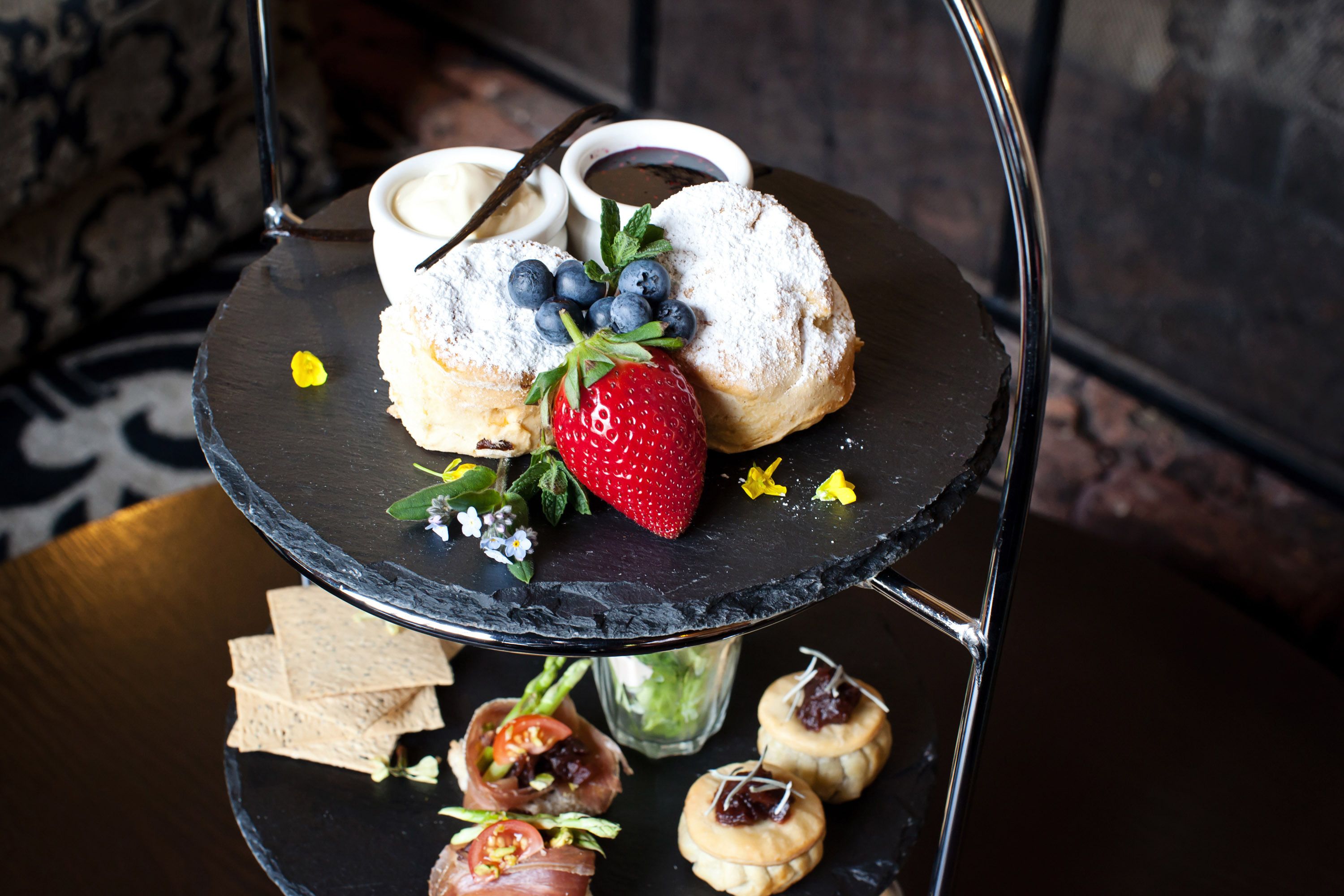 A three-tiered serving tray with pastries, a strawberry, and a small bowl of cream.