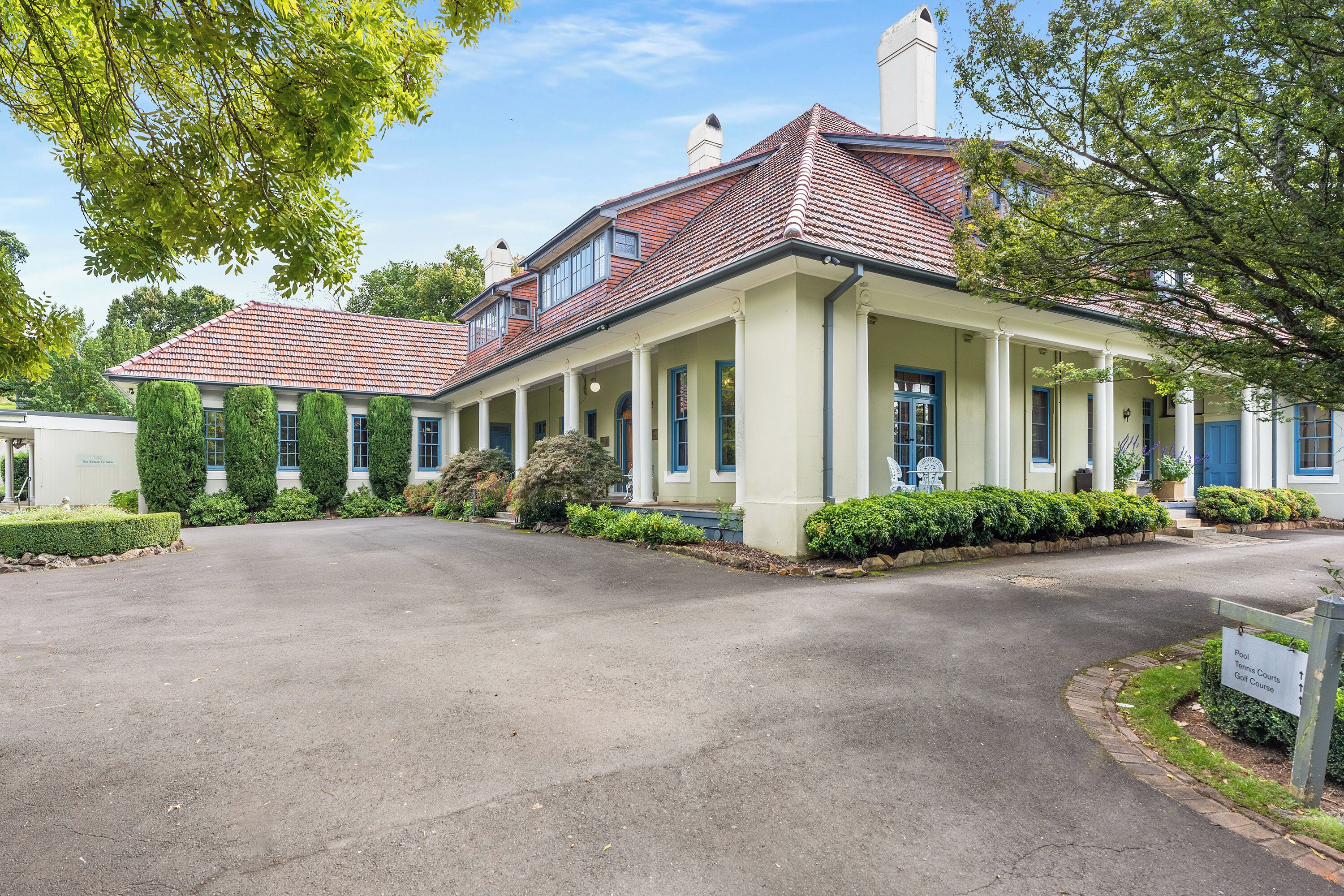 A two-story building with a red-tiled roof, a covered porch with columns, and a sign indicating it is a golf course clubhouse.