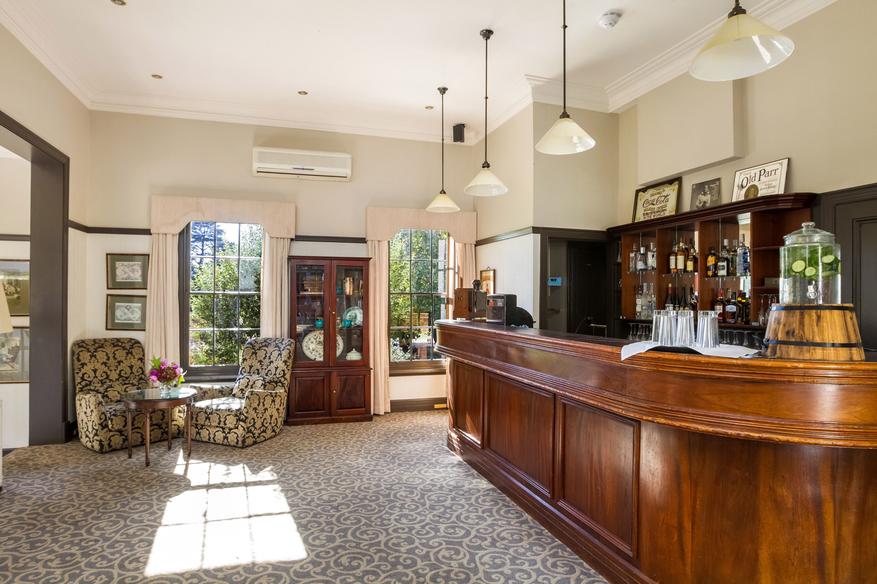 Una zona de bar con mostrador de madera, taburetes y un ventanal con cortinas.
