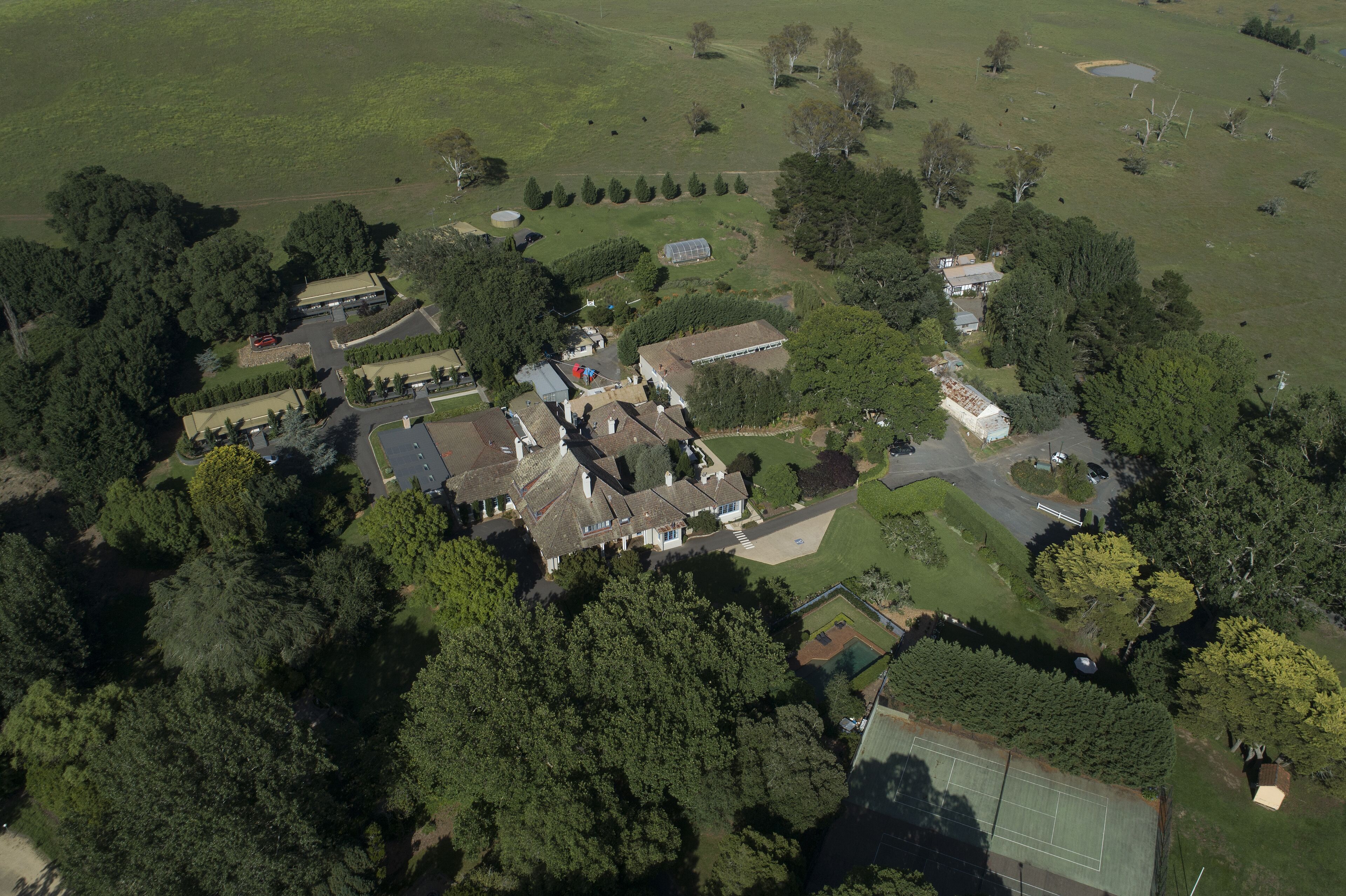 An aerial view of a residential area with multiple houses, a tennis court, and a large green field.