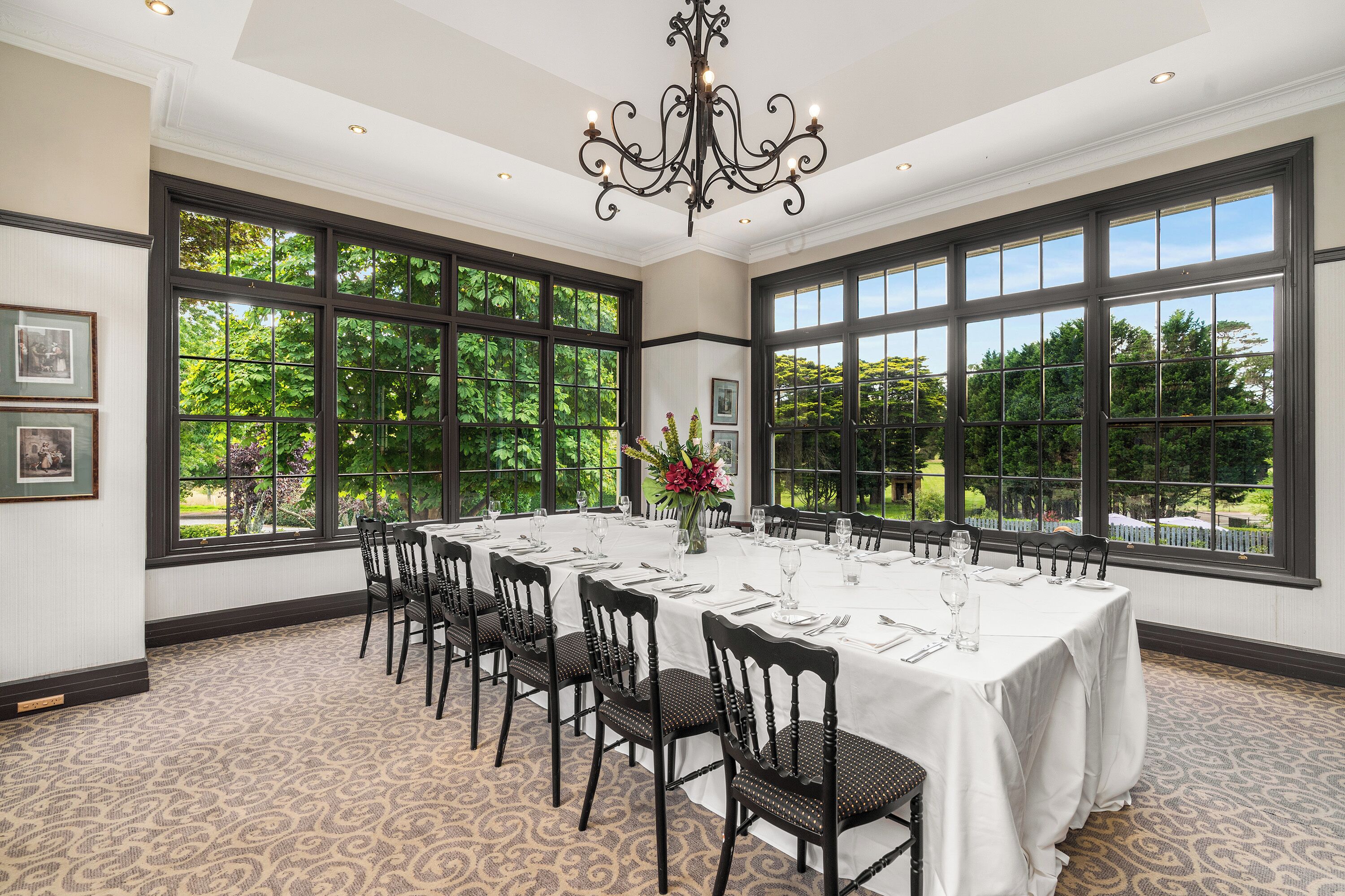 A dining room with a long table set for a meal, large windows, and a chandelier.