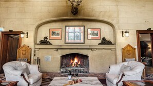 A room with a fireplace, two armchairs, a table with a bottle of wine, and a plate of food. - Peppers Manor House (Sutton Forest)