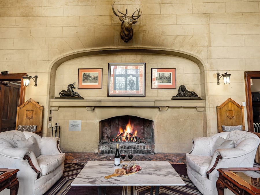 A room with a fireplace, two armchairs, a table with a bottle of wine, and a plate of food.