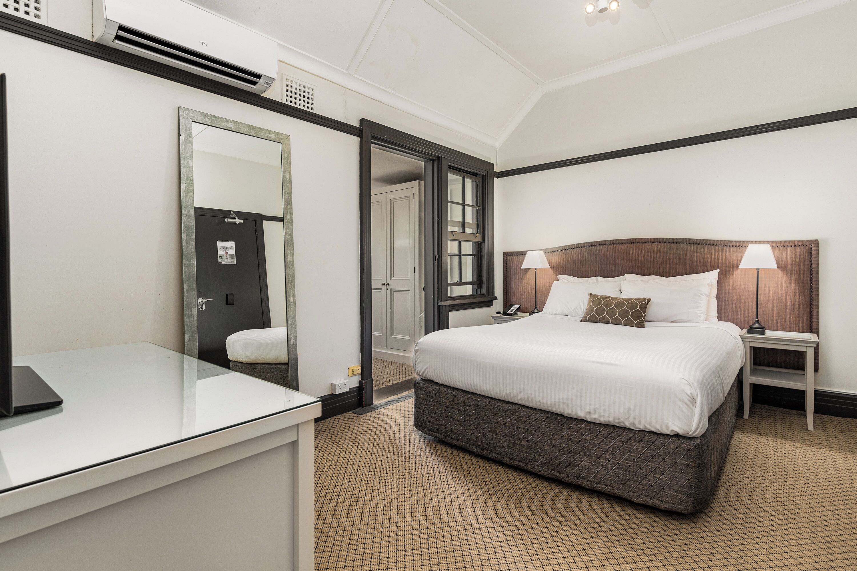Una camera d'albergo con un letto, un comodino, una lampada e uno specchio.