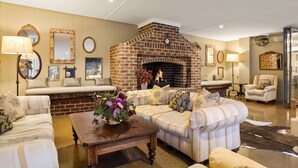 A cozy living room with a brick fireplace, striped sofas, and a coffee table with flowers. - Peppers Manor House (Sutton Forest)