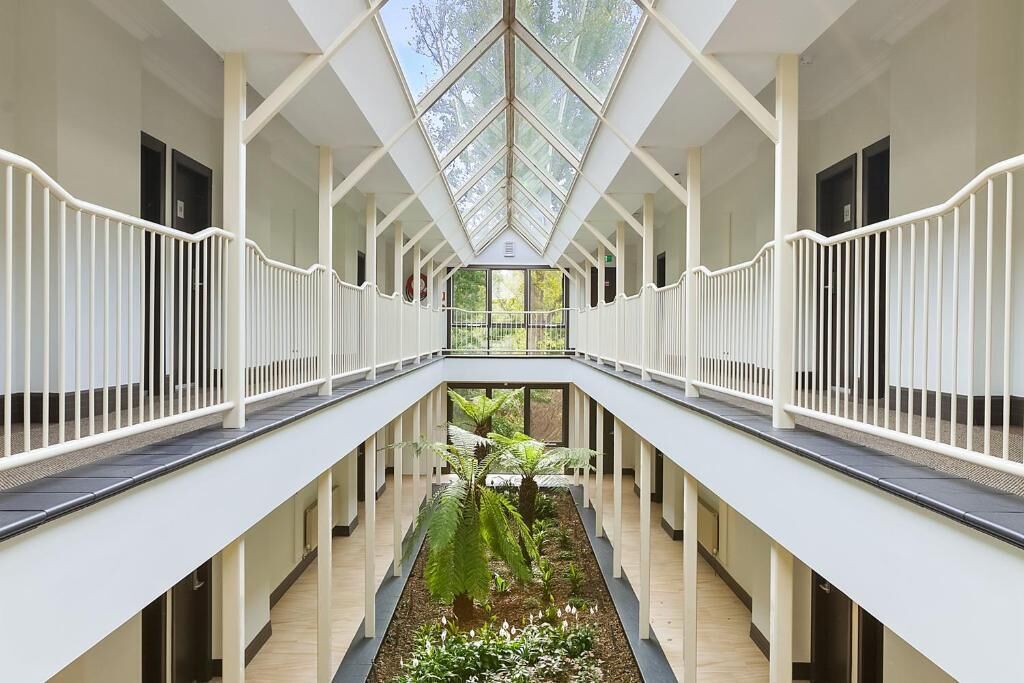 A multi-level atrium with a central garden, white railings, and a glass ceiling.