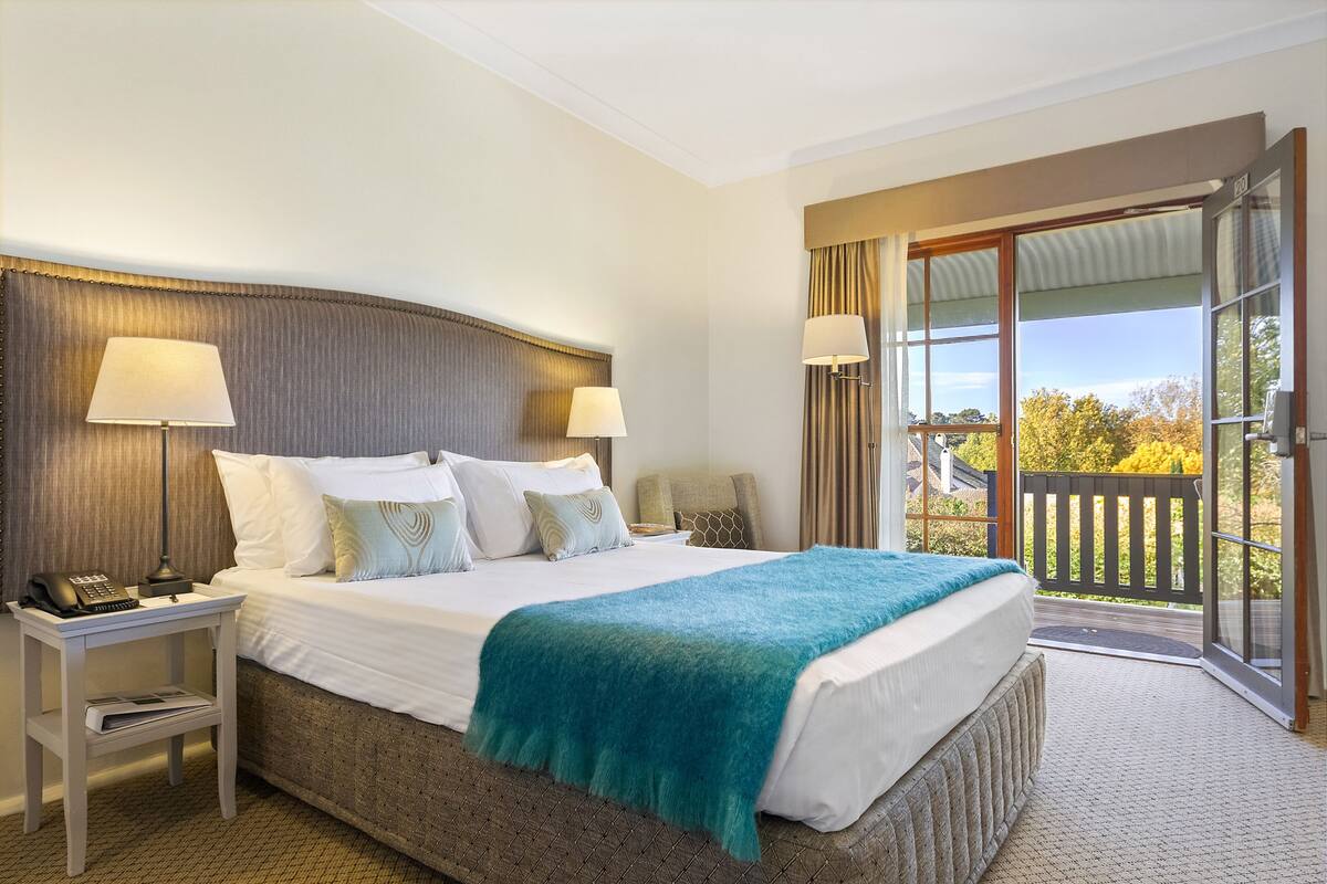 Habitación de hotel con una cama grande, dos lámparas de noche, un teléfono y vista al exterior a través de una puerta corrediza de vidrio.