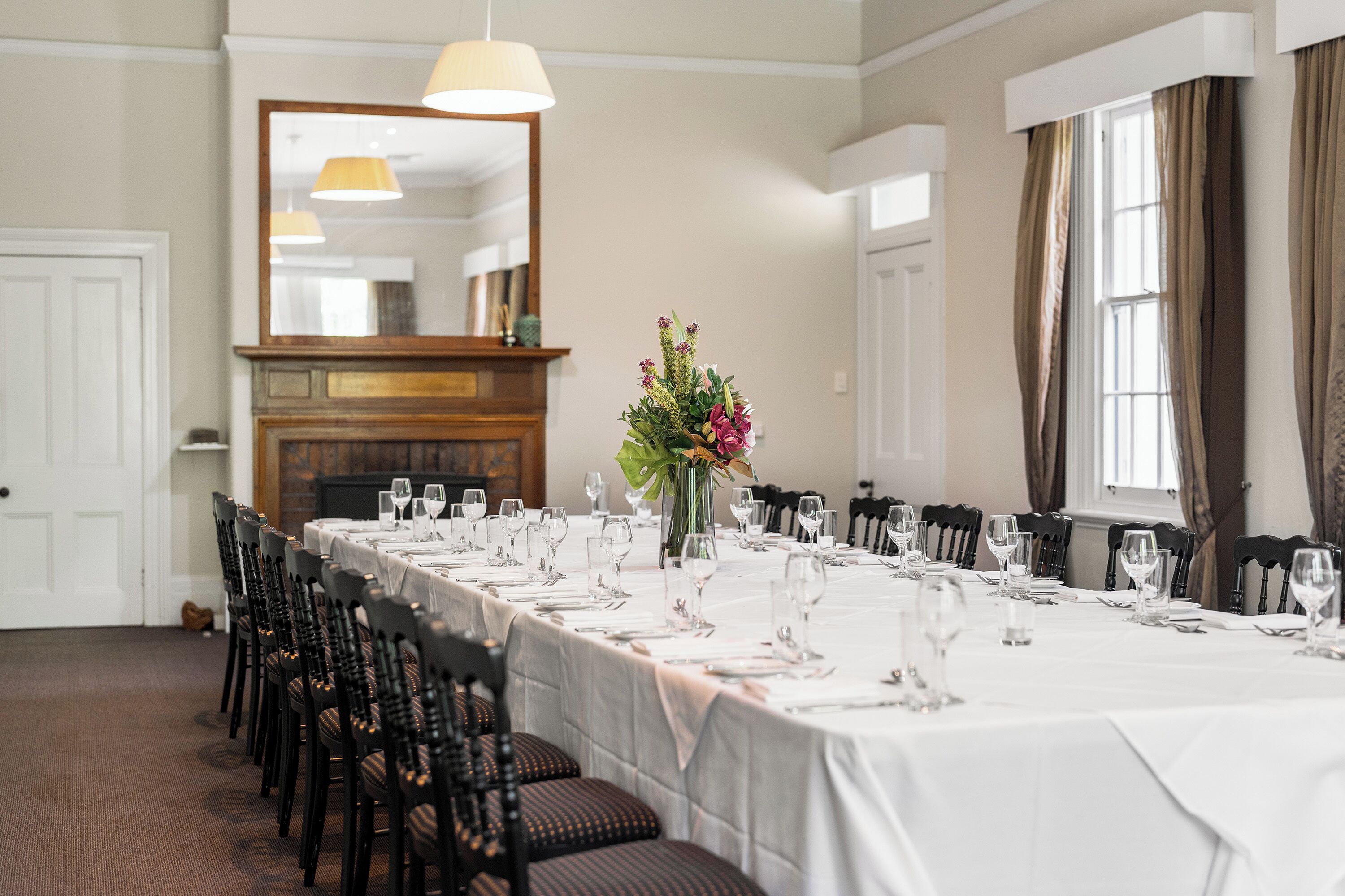 A long dining table set for a meal with chairs, a vase of flowers, and a mirror above.