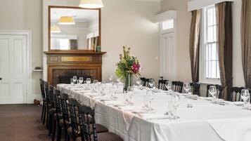 A long dining table set for a meal with chairs, a vase of flowers, and a mirror above.