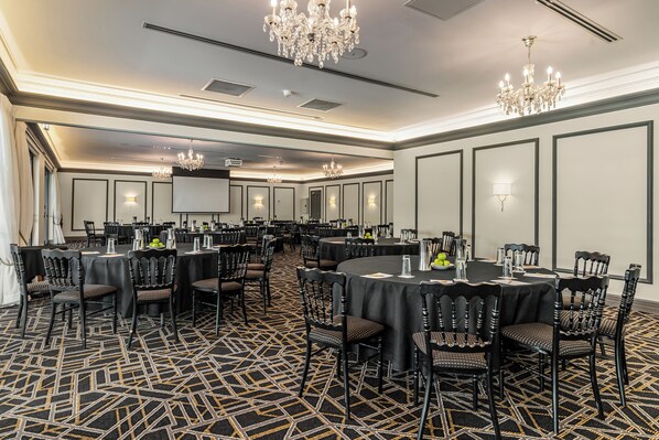Une salle de conférence dotée de plusieurs tables et chaises, de lustres et d’un grand écran.