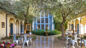 An outdoor café with tables and chairs, a fountain, and a building with blue-framed windows in the background. - Peppers Manor House (Sutton Forest)