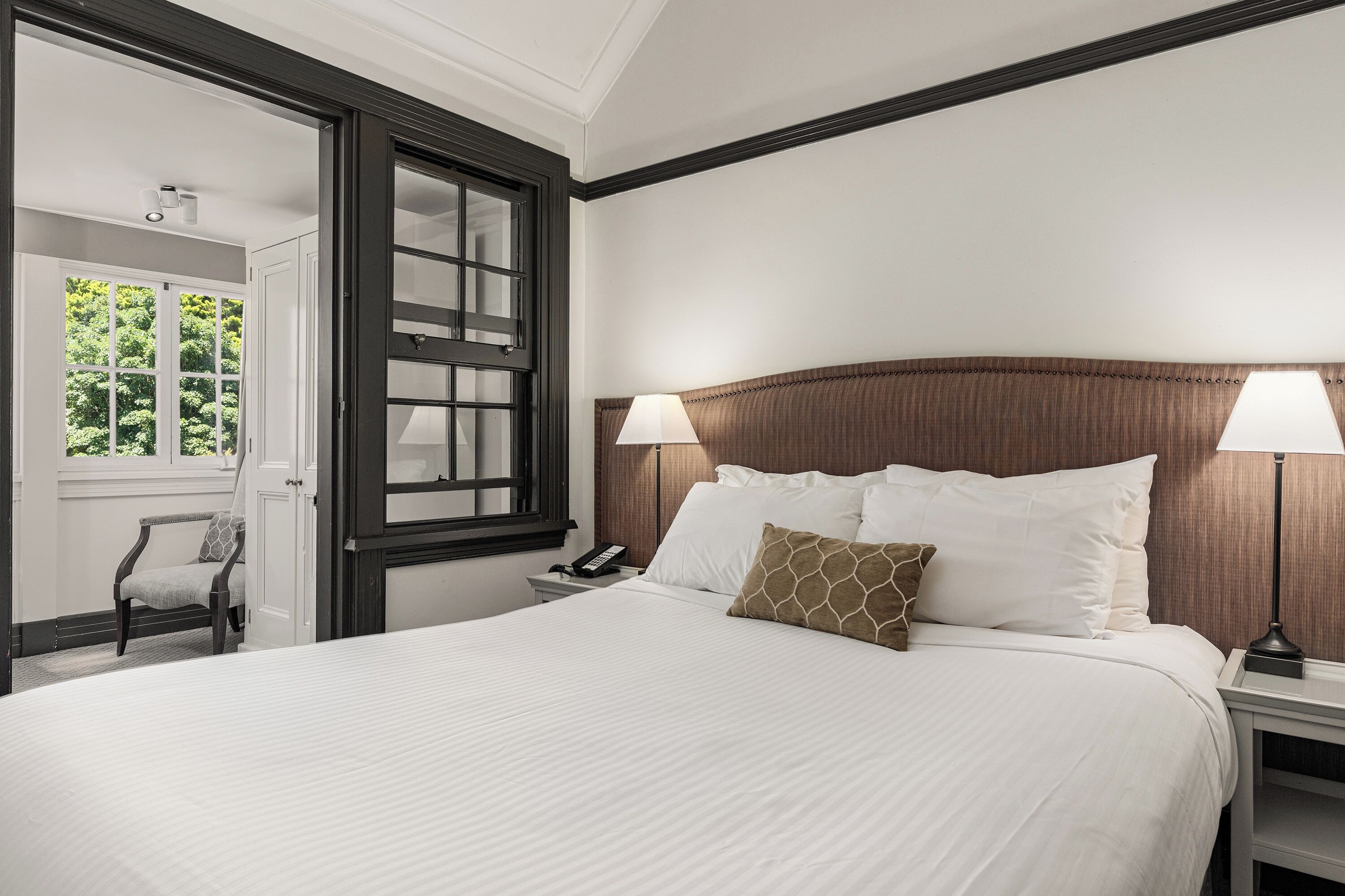 A neatly made bed with white linens, a wooden headboard, and two bedside lamps.