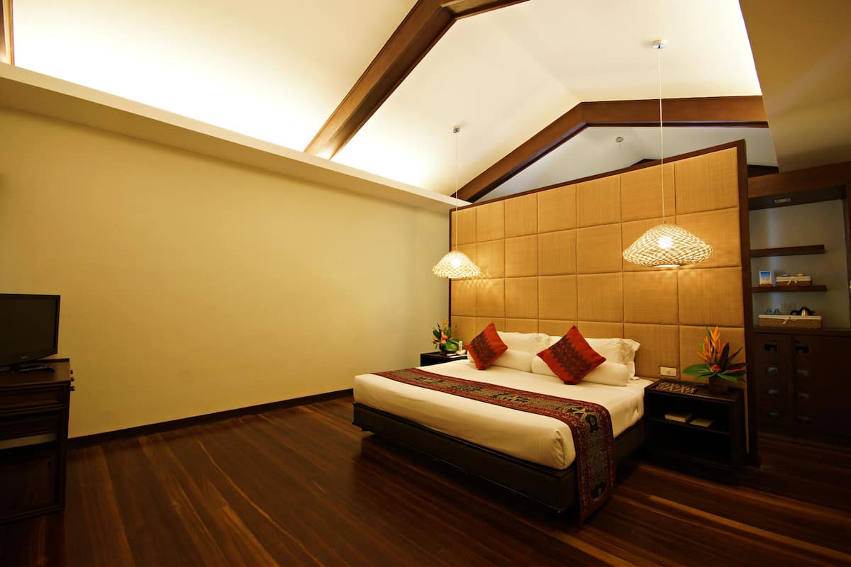 A modern hotel room with a large bed, wooden flooring, a TV, and a skylight.