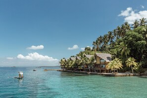 Una propiedad frente a la playa con estructura de madera, palmeras y agua azul cristalina.
