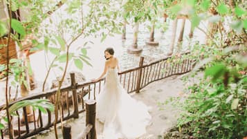 Bride stands on a serene garden pathway surrounded by lush greenery and a charming fence.