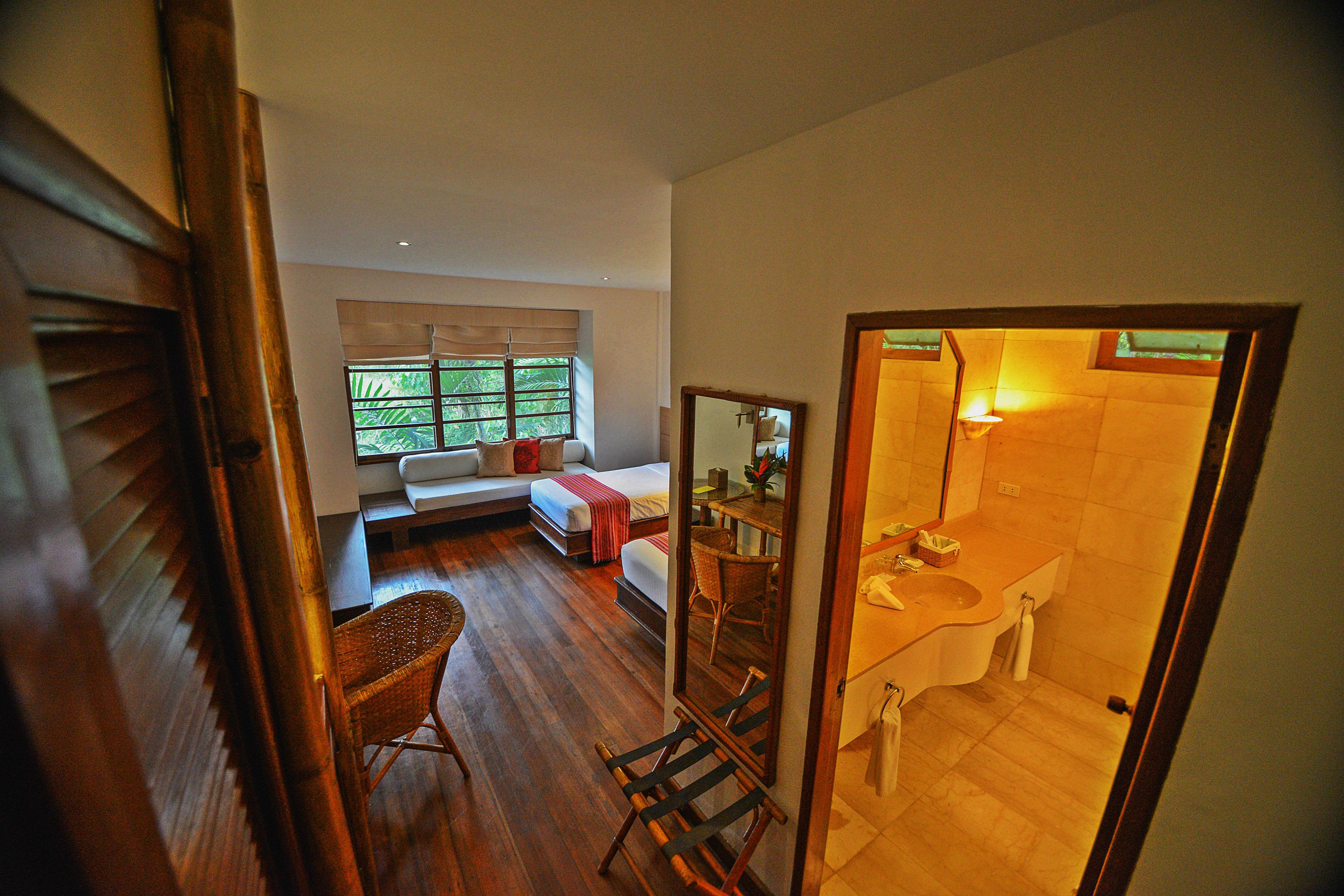 A room with a bed, a window, a chair, and a bathroom with a sink and mirror.