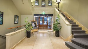 A hotel lobby with a staircase, a reception desk, and framed pictures on the walls.