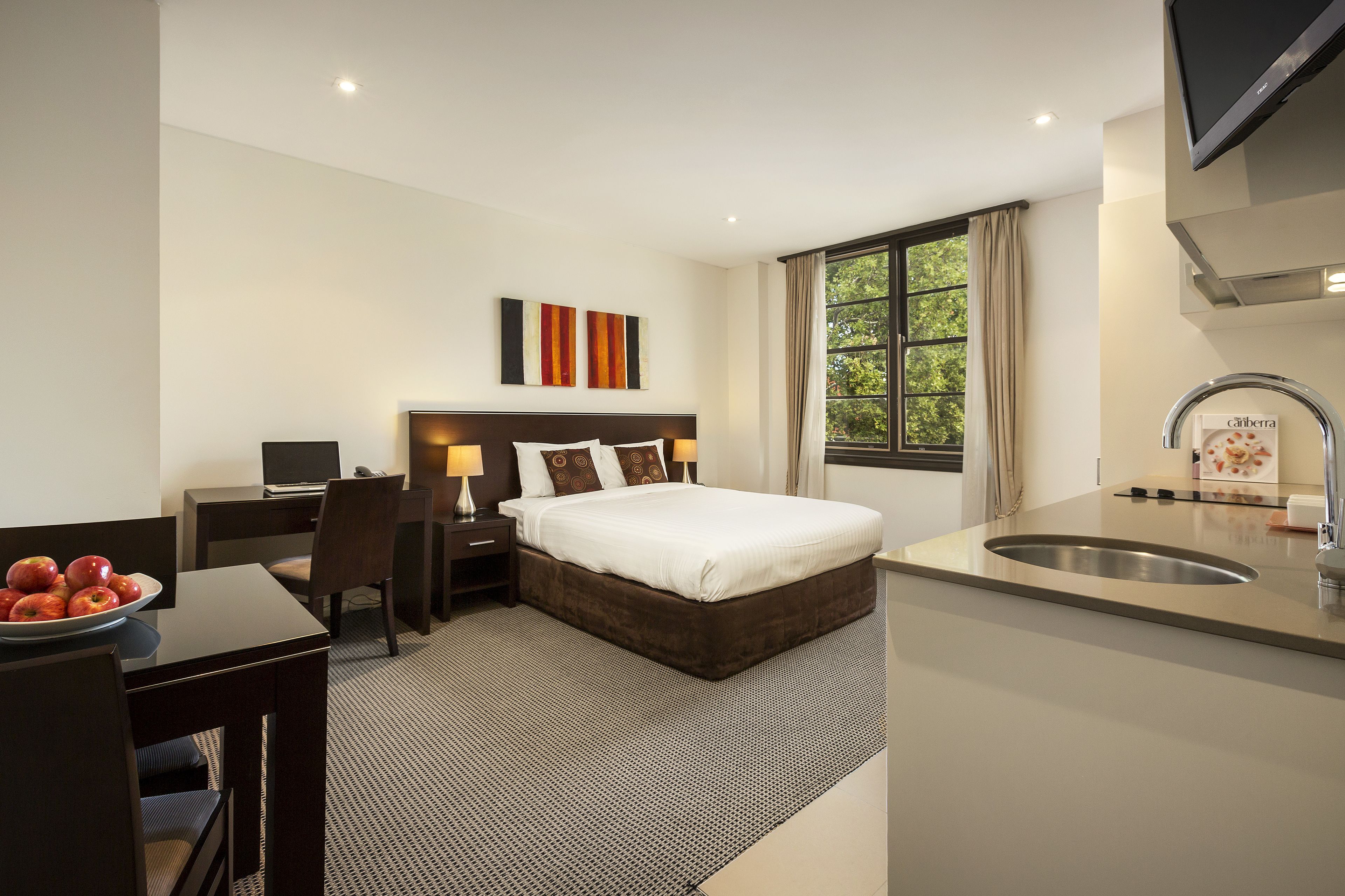 A hotel room with a bed, desk, chair, and a small kitchenette.