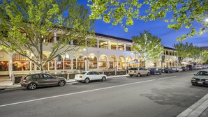 A street lined with parked cars and a building with arched windows and a covered walkway.
