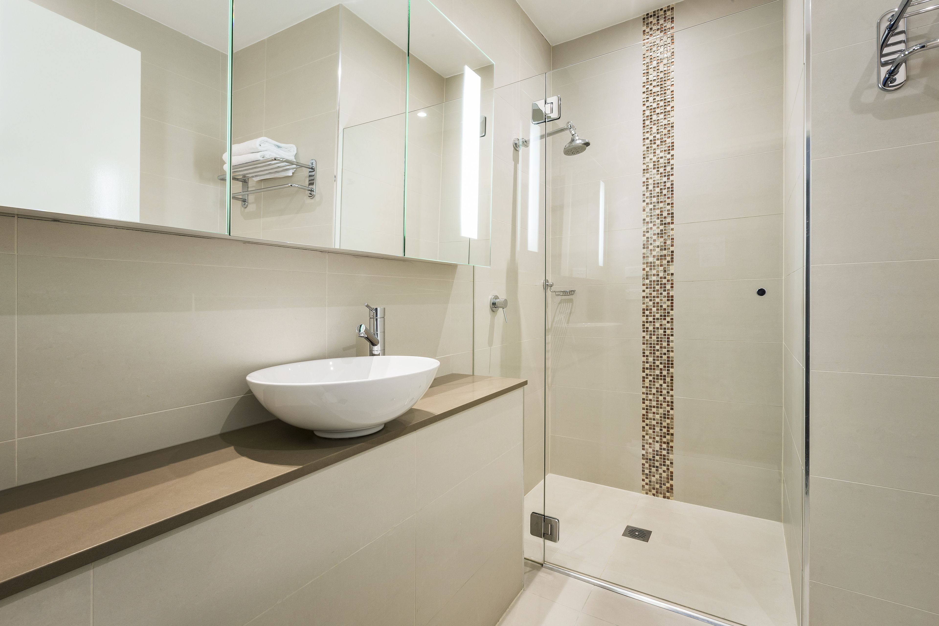 A modern bathroom with a large mirror, a white sink, and a glass-enclosed shower area.