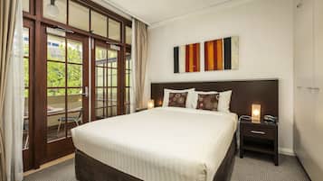 A hotel room with a large bed, a nightstand, a wall-mounted artwork, and a sliding glass door leading to an outdoor area.