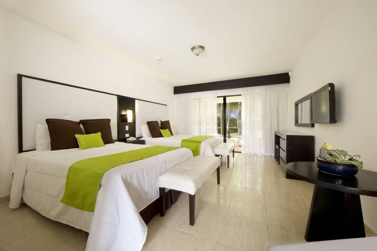 A hotel room with two beds, a desk, a TV, and a window with curtains.