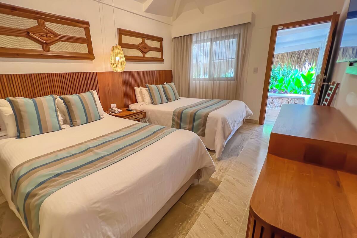 A hotel room with two beds, wooden headboard panels, a nightstand, and a large window with curtains.