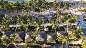 Eine Vogelperspektive zeigt ein Resort mit strohgedeckten Cabanas, Palmen und einen Strand.