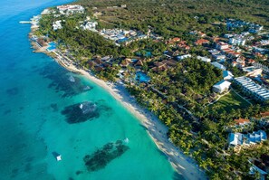 Vista aérea de un resort costero con propiedades frente a la playa, aguas turquesas cristalinas y exuberante vegetación.