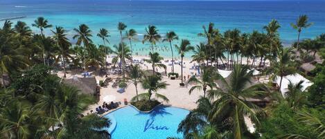 A beach resort with a swimming pool, palm trees, and a view of the ocean.