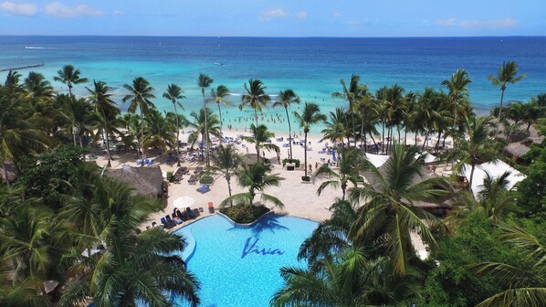 Un resort en la playa con piscina, palmeras y vistas al océano.