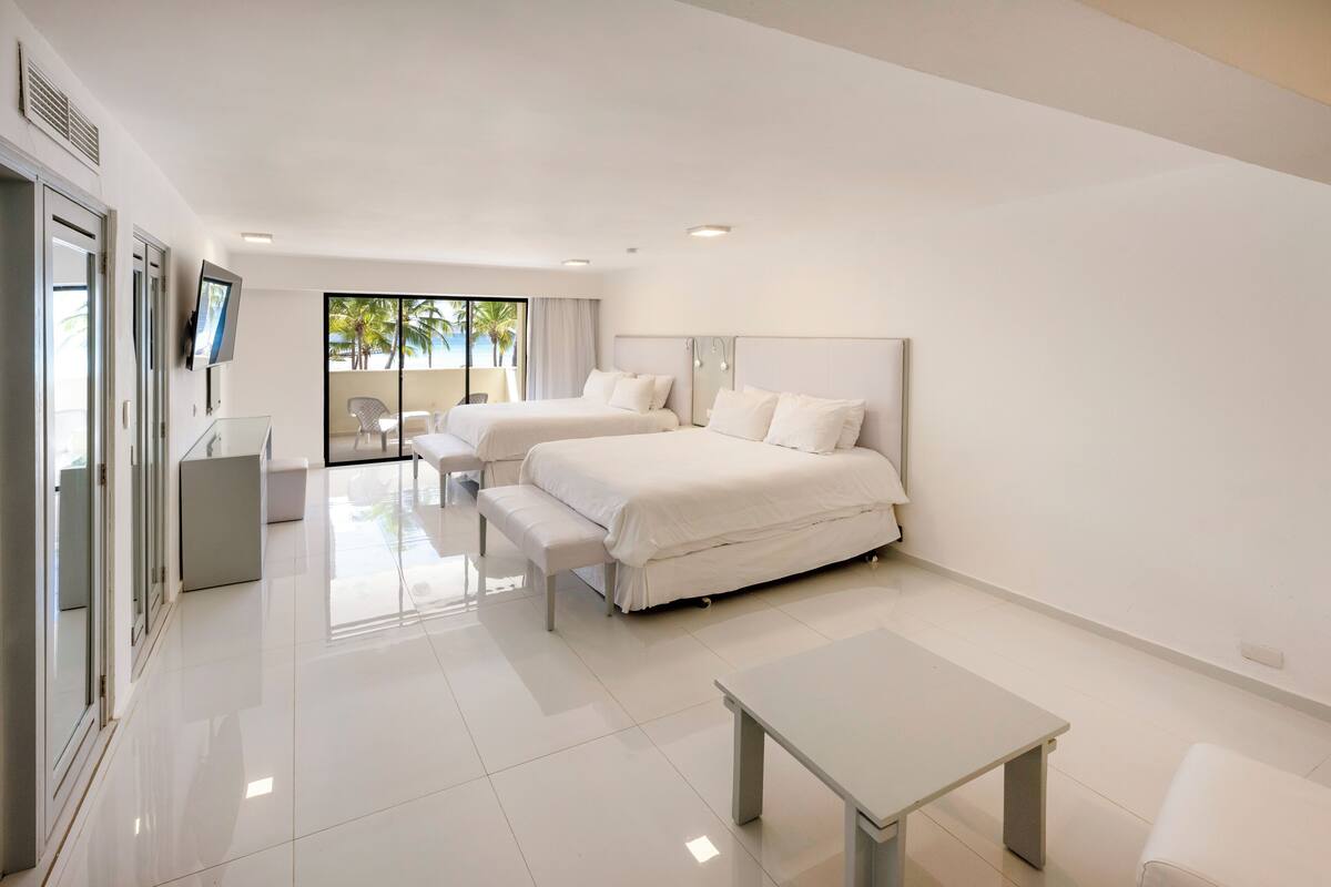 A modern hotel room with two beds, a desk, and a bench.