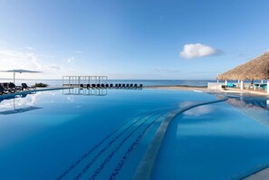 Una piscina infinita de color azul cristalino con sillas de descanso y sombrillas, con vistas al océano.